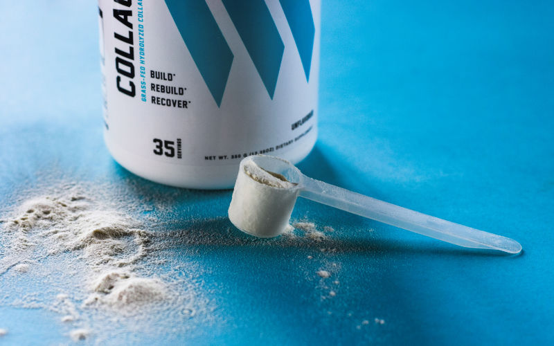 Swolverine collagen container sitting on blue surface with full scoop of collagen powder in front.