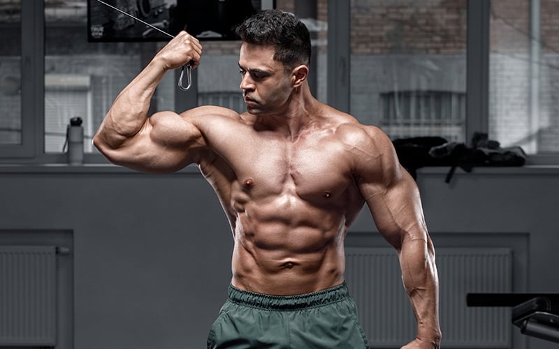 Shirtless muscular man flexing biceps in the gym